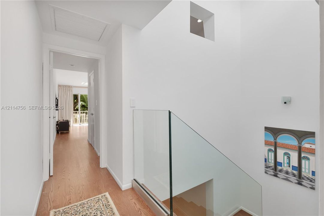 Staircase featuring a frameless glass railing, wood-finish flooring, and high-reaching ceilings with a recessed architectural niche