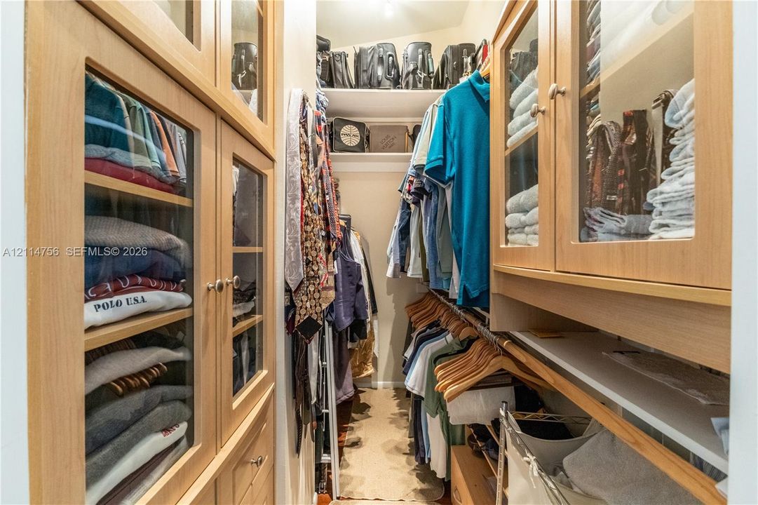Walk-in closet featuring custom wood-finish cabinetry, glass-front upper storage doors, integrated shelving, and multi-tier hanging rods