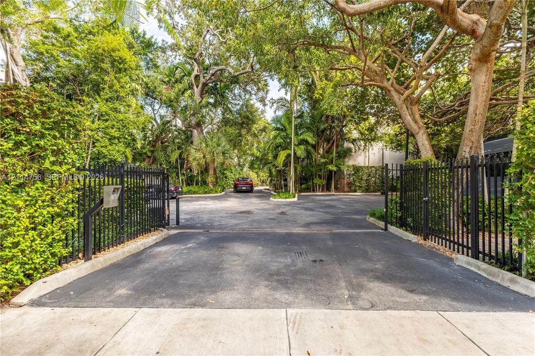 Gated entrance featuring black metal perimeter fencing and mature trees