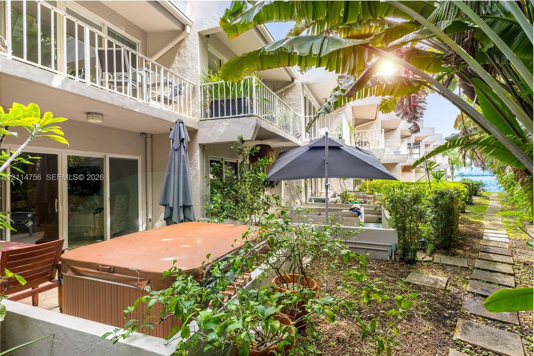 Exterior patio space featuring a hot tub, multiple levels of private balconies with white railings, and a stone paver path