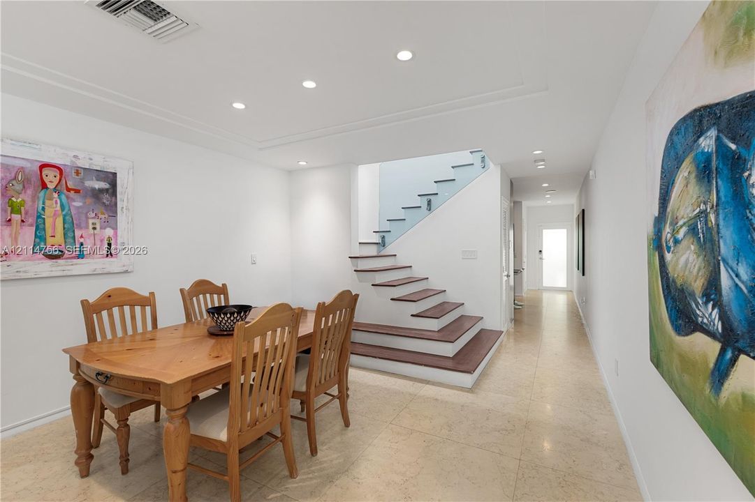Open-plan interior featuring stone flooring, recessed ceiling lighting, and a staircase with wood-finish treads and a glass panel railing