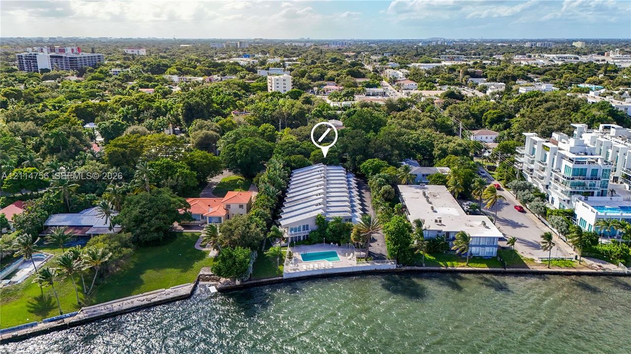 Waterfront property featuring a bulkhead-lined shoreline, a rectangular swimming pool, and mature perimeter landscaping