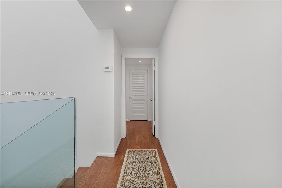 Hallway featuring wood-finish flooring, recessed lighting, and a glass panel railing