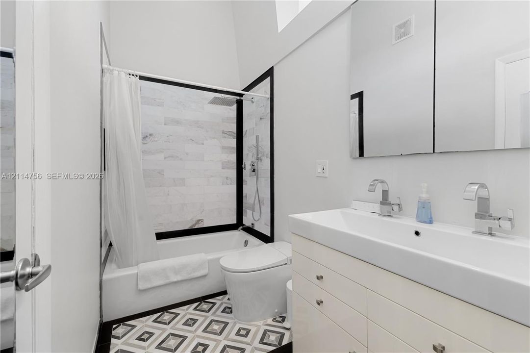Bathroom featuring a white vanity with an integrated dual-faucet sink, tiled shower surround with black framing, geometric patterned floor tile, and a wall-mounted mirrored medicine cabinet