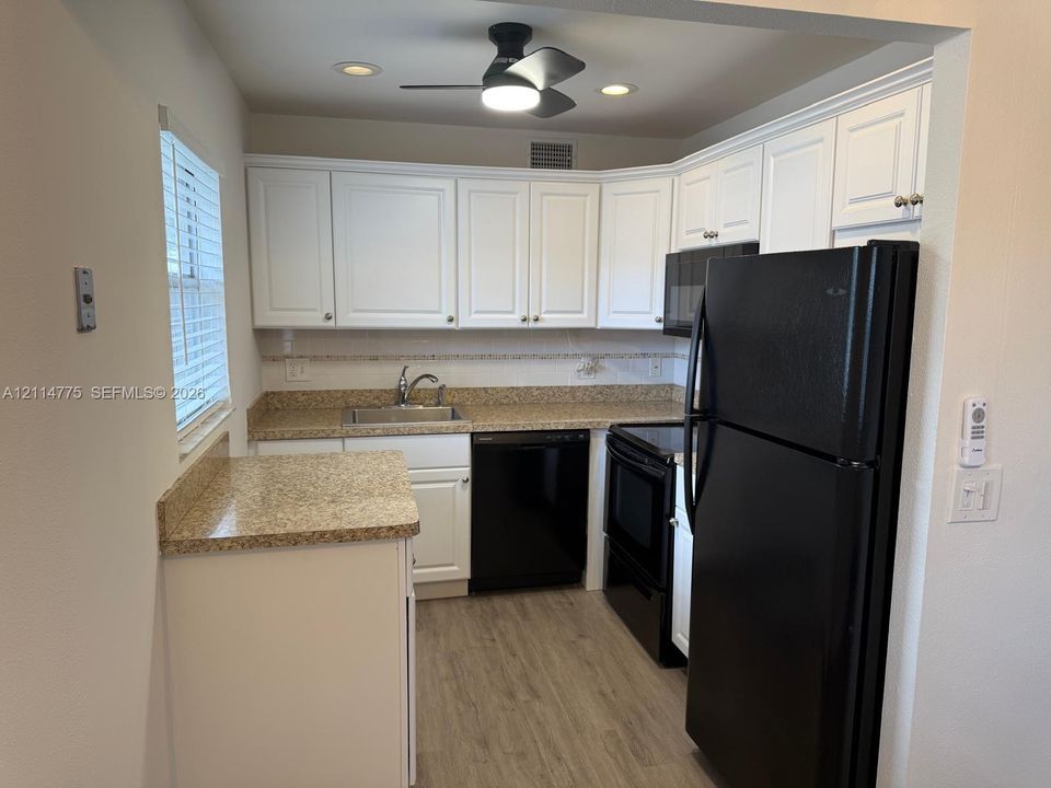 Kitchen featuring white cabinetry, stone-finish countertops, black appliances, recessed lighting, and wood-finish flooring