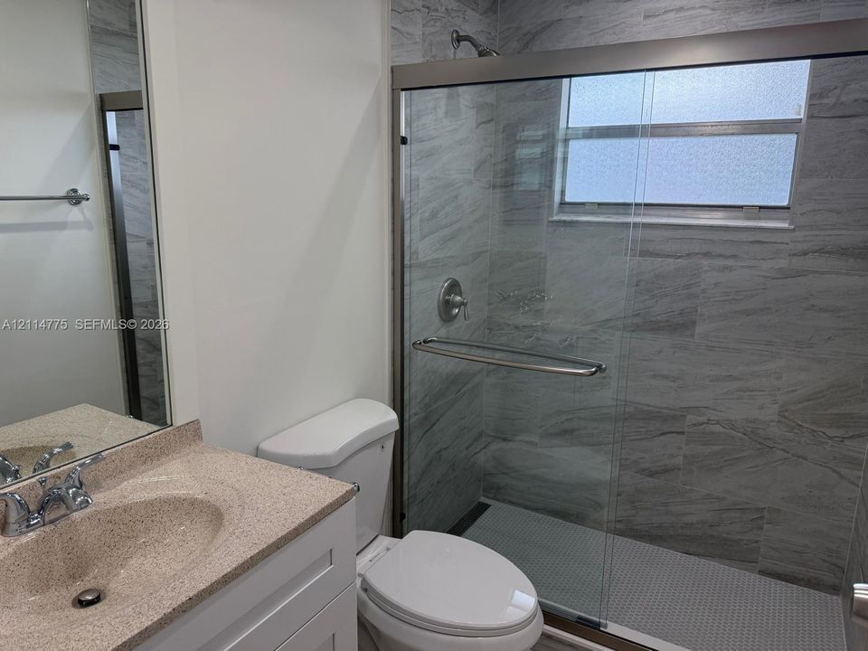 Bathroom featuring a vanity with a neutral-toned countertop, a frameless glass-enclosed shower, floor-to-ceiling stone-patterned wall tile, and a built-in towel bar