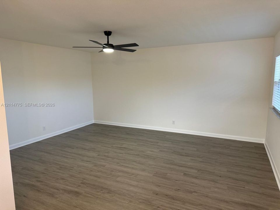 Neutral-toned interior space featuring wood-finish flooring and a central matte black ceiling fan with integrated lighting