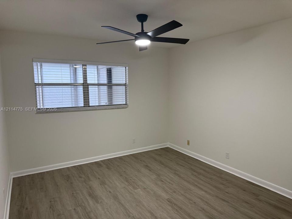 Room featuring wood-finish flooring, a matte black ceiling fan with integrated lighting, and a multi-pane window with installed blinds
