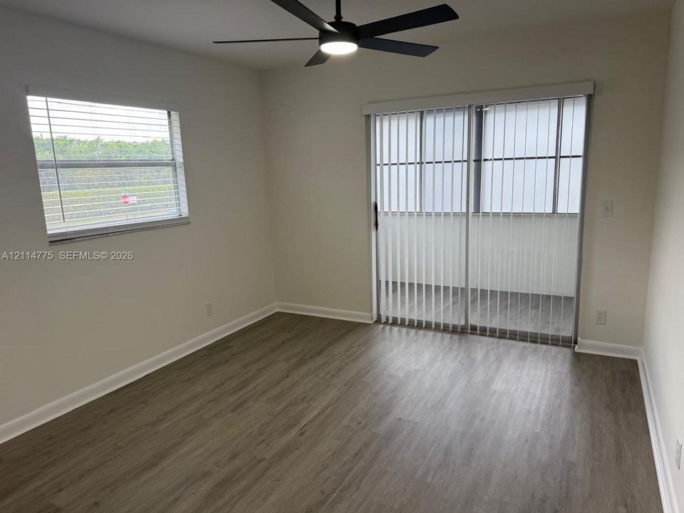 Room featuring wood-finish flooring, a matte black ceiling fan with integrated lighting, horizontal window blinds, and sliding glass doors with vertical blinds