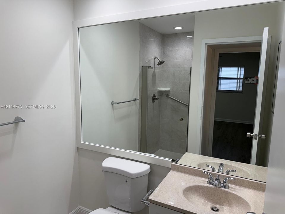Bathroom featuring a vanity with a solid-surface countertop, an integrated sink, a large wall-mounted mirror, and a walk-in shower with stone-finish wall tile