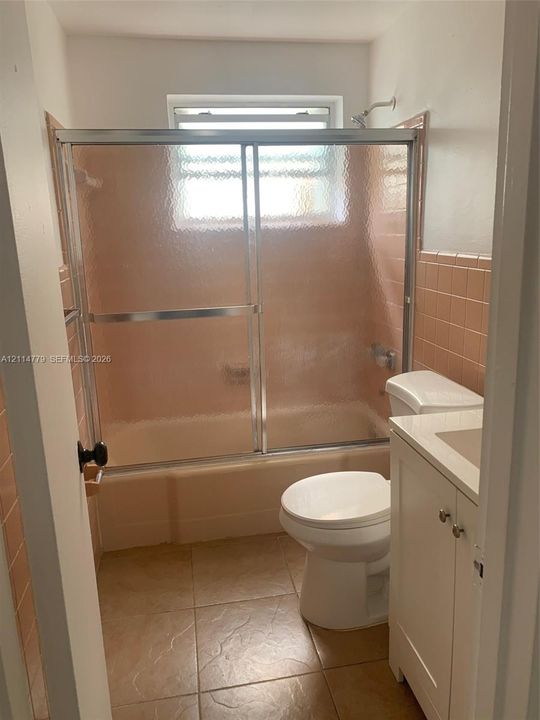 Bathroom featuring a tiled tub surround, sliding glass shower door, integrated vanity cabinet with a stone-finish countertop, and floor tiling