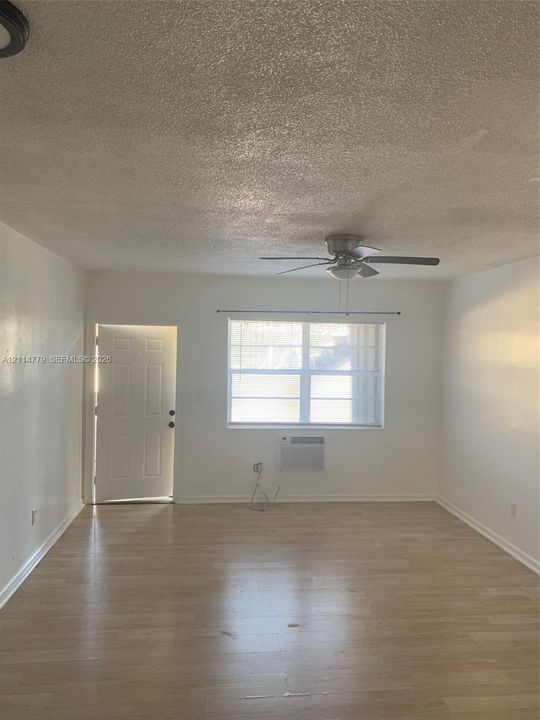 Wood-finish flooring, ceiling fan with integrated light fixture, and window with built-in wall-mounted air conditioning unit