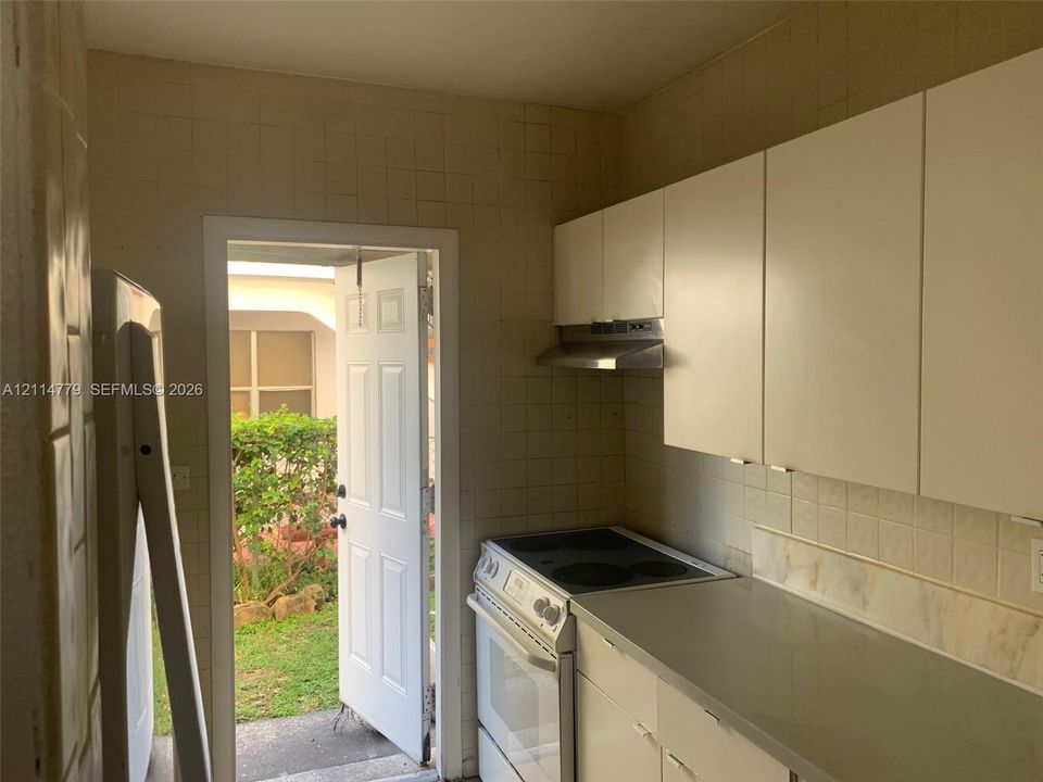 Kitchen featuring flat-panel white cabinetry, solid-surface countertops, electric range, stainless steel vent hood, and tiled wall surfacing