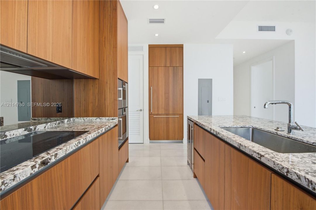 Kitchen featuring custom wood cabinetry, stone countertops, panel-ready refrigerator, stainless steel undermount sink with chrome faucet, and integrated wall oven