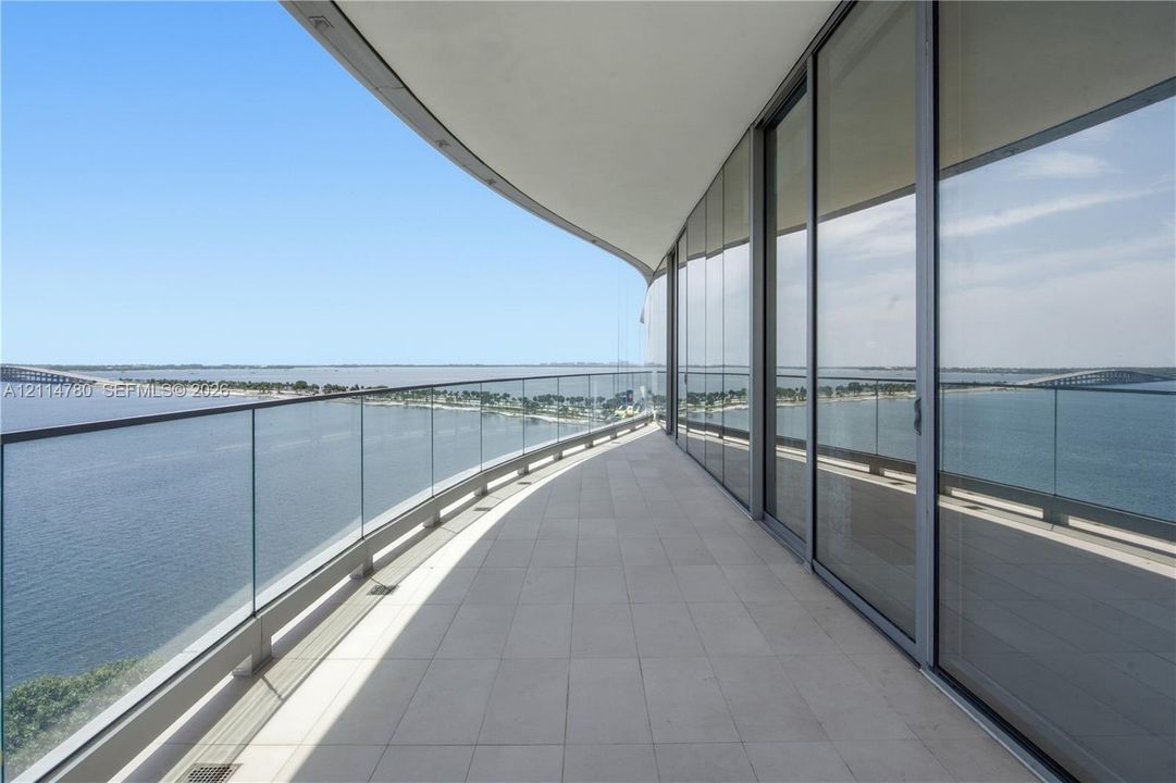 Curved balcony featuring stone tile flooring, a transparent glass railing, and floor-to-ceiling glass sliding doors
