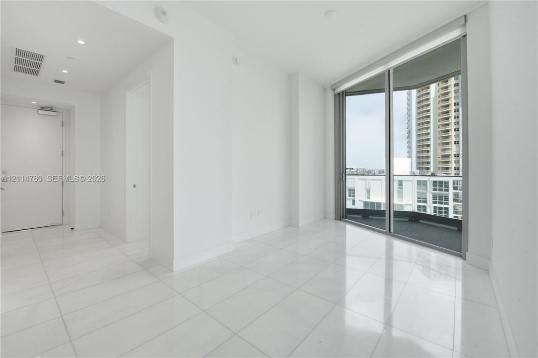 Minimalist interior featuring white tile flooring, recessed lighting, and floor-to-ceiling glass sliding doors opening to a balcony