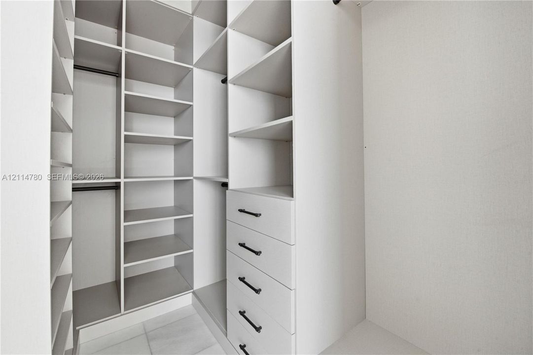 Custom walk-in closet featuring extensive built-in white shelving, integrated hanging rods, a tiered drawer stack, and matte black hardware