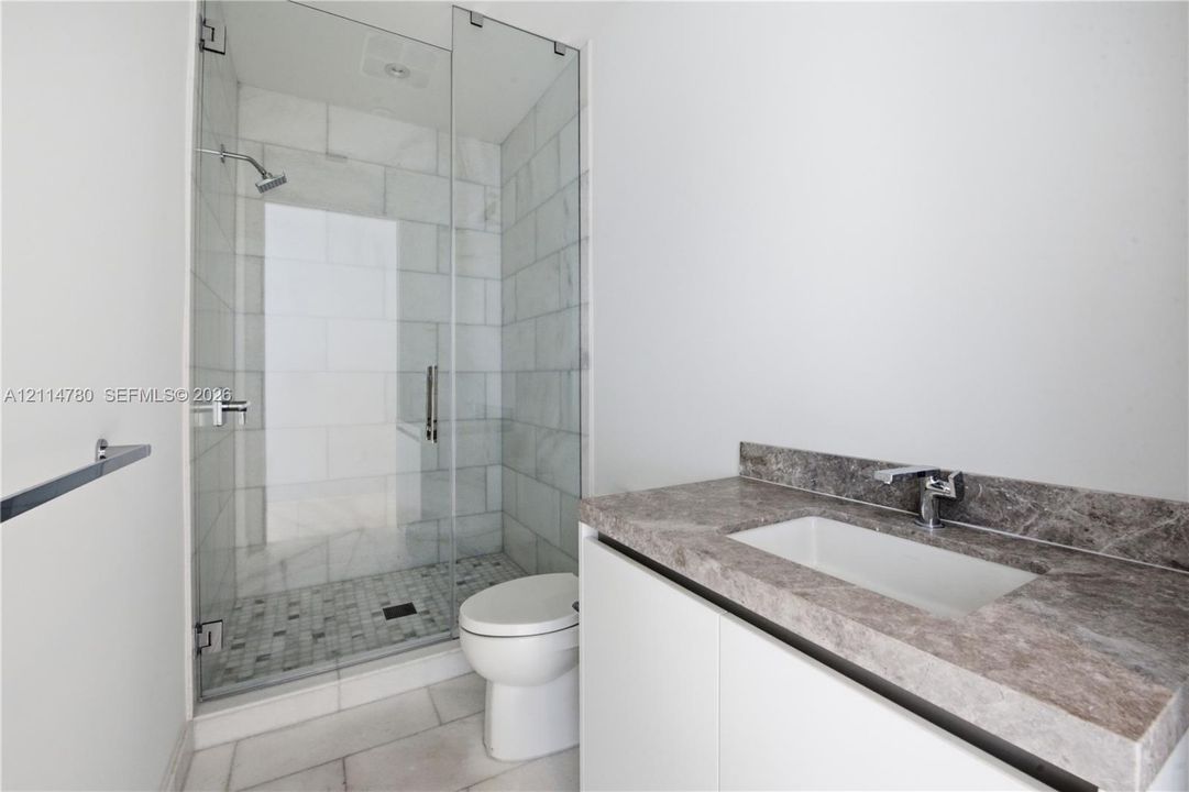 Walk-in glass-enclosed shower featuring large-format tile surround and mosaic tile floor, stone-finish countertop, integrated undermount sink, and minimalist cabinetry