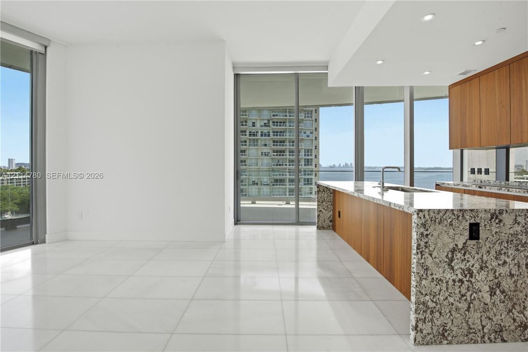 Open-concept space featuring floor-to-ceiling windows, light-toned tile flooring, recessed lighting, wood-finish cabinetry, and stone-surfaced kitchen countertops