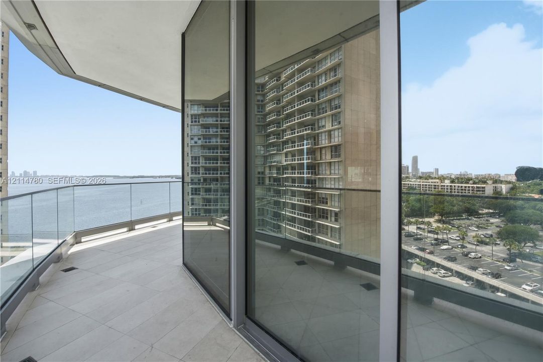 Covered balcony with large-format tile flooring and a frameless glass railing system, featuring floor-to-ceiling glass sliding doors