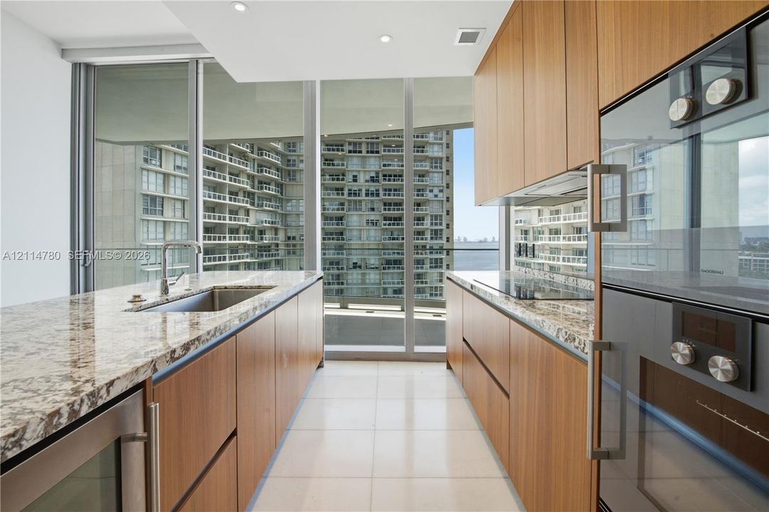 Kitchen featuring wood-finish flat-panel cabinetry, stone countertops, integrated cooktop, built-in double oven, and floor-to-ceiling glass windows