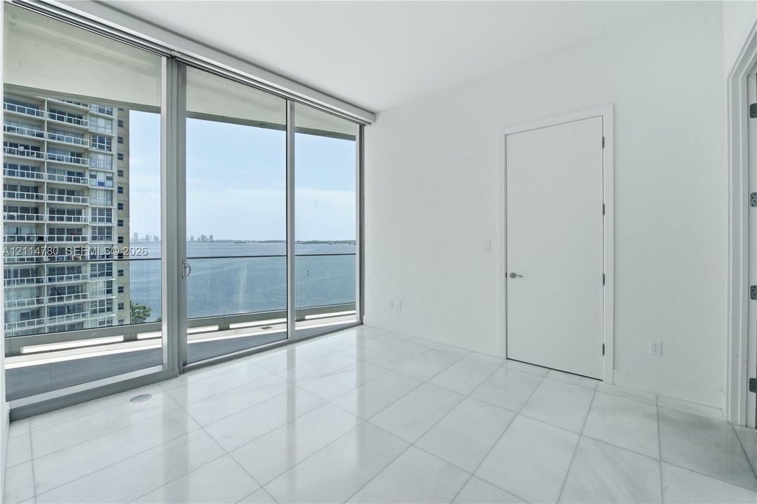 Floor-to-ceiling windows, large-format tile flooring, glass balcony railing, and water backdrop