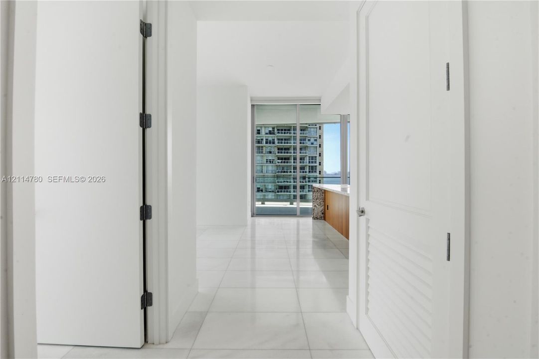 Interior hallway featuring large-format tile flooring, white slab doors, and a full-height glass door