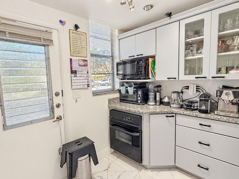 Kitchen featuring white cabinetry with glass-front uppers, speckled stone countertops, black integrated oven, built-in microwave, and tile flooring