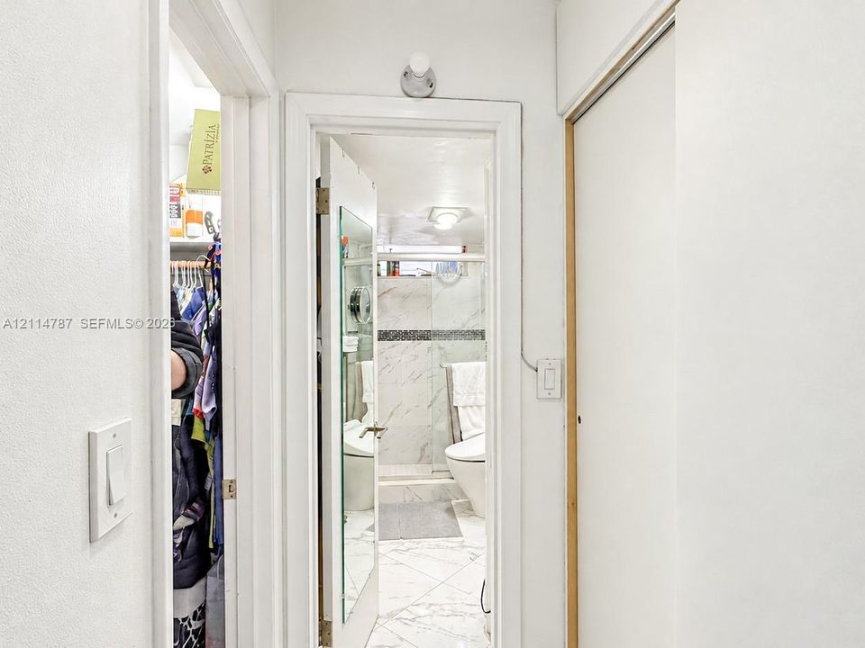 Bathroom featuring stone-finish wall and floor tiling, a glass-enclosed shower, a wall-mounted light fixture, and floor-to-ceiling closet cabinetry