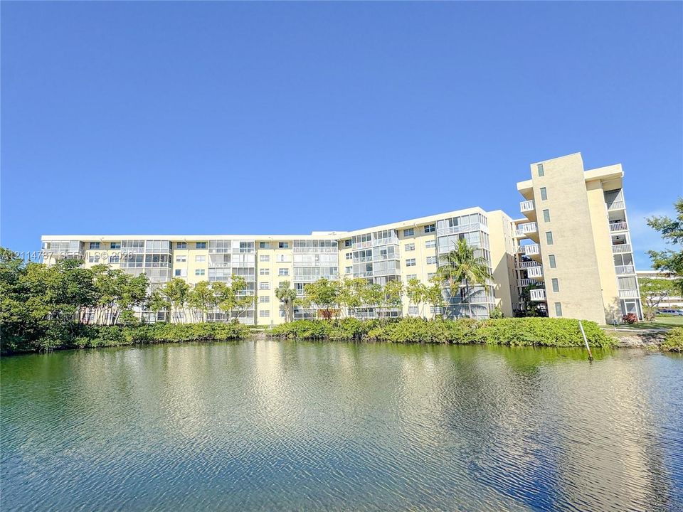 Multi-story residential building featuring private screened balconies, exterior facade with neutral finish, and a prominent water feature with landscaped vegetation