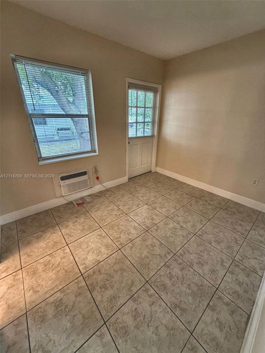 Room featuring large-format ceramic tile flooring, a window with horizontal blinds, a single-lite glass panel door, and an integrated wall-mounted air conditioning unit