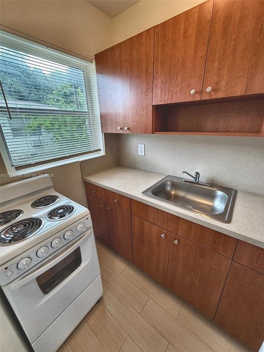 Kitchen featuring wood-finish cabinetry, solid-surface countertops, an integrated stainless steel sink with a deck-mounted faucet, a white electric range, and wood-finish flooring