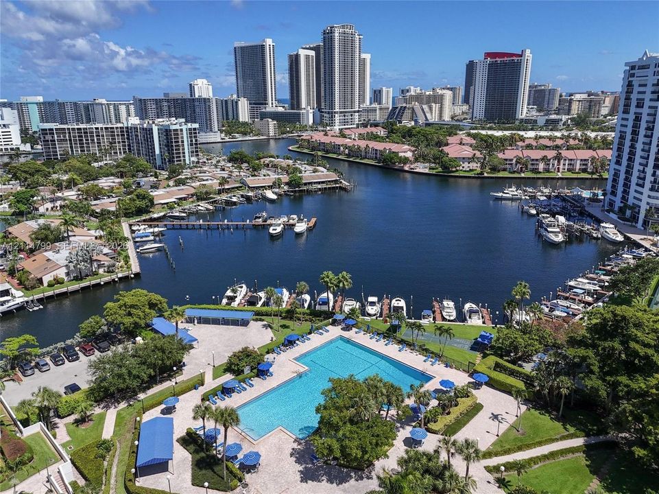 Rectangular swimming pool with paved decking, surrounding landscaping, marina access, and metropolitan skyline backdrop