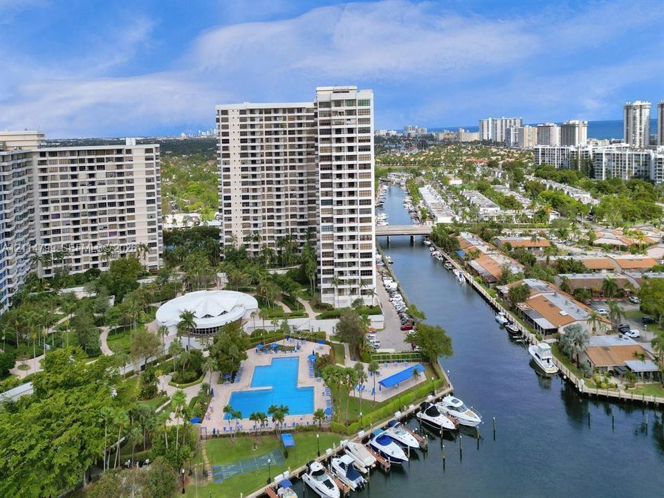 Aerial perspective of high-rise residential complex featuring a community swimming pool, canal-front boat slips, and landscaped grounds