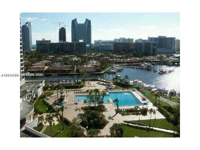 Aerial perspective featuring a waterfront swimming pool, paved pool deck, manicured green space, and maritime slips