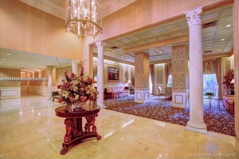 Grand entrance hall featuring polished stone flooring, ornate classical columns, recessed ceiling lighting, and a tiered hanging chandelier