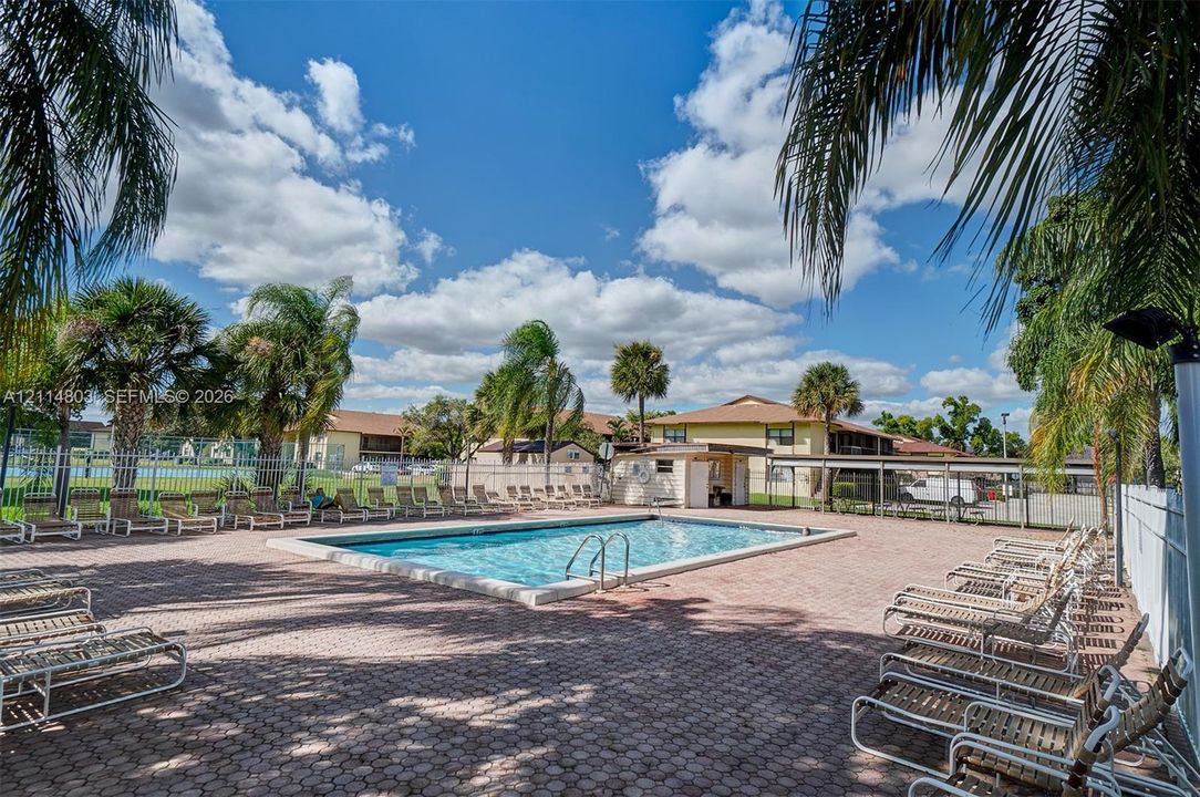 Outdoor swimming pool featuring a brick-paver deck, perimeter fencing, and mature palm trees