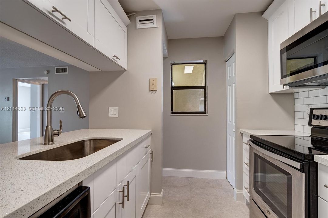 Kitchen featuring white shaker-style cabinetry, quartz countertops, stainless steel appliances, and white subway tile backsplash