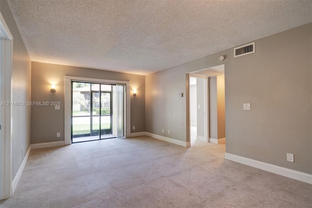 Neutral-toned interior space featuring large-format tile flooring, wall-mounted light fixtures, and a sliding glass door providing external access