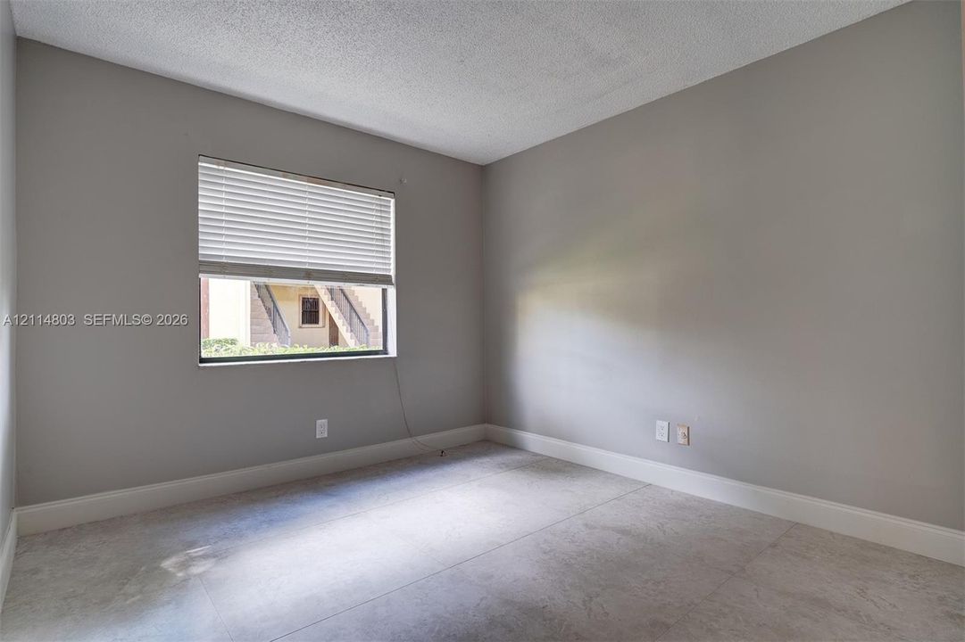 Neutral-toned interior space featuring light-colored stone-finish flooring, textured ceiling finish, and a window with fitted horizontal blinds
