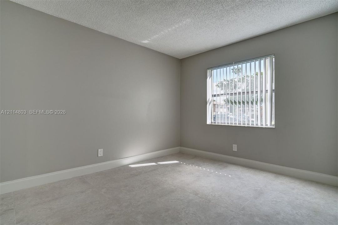 Neutral-toned interior space featuring light-colored tile flooring, textured ceilings, and a window with vertical blinds