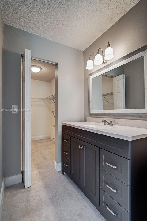 Dark-toned vanity with multi-drawer storage, light-colored stone-finish countertop, integrated sink, framed rectangular wall mirror, and three-bulb vanity lighting fixture