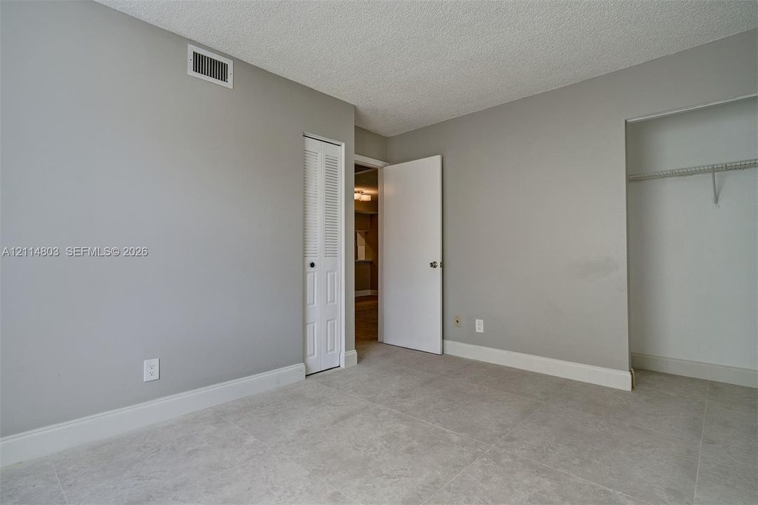 Interior space featuring large-format ceramic tile flooring, neutral grey wall paint, a built-in closet with wire shelving, and louvered bifold doors