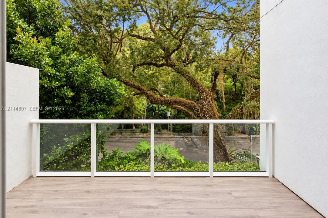 Covered balcony with wood-finish flooring, white railing, and glass panel inserts
