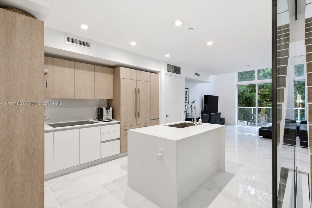 Kitchen featuring light wood-finish cabinetry, a white stone-surface island, built-in panel-ready refrigerator, and polished stone-finish flooring with floor-to-ceiling windows
