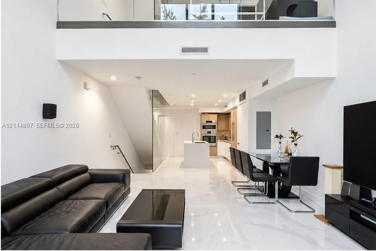Double-height ceiling, polished tile flooring, glass mezzanine railing, stainless steel built-in appliances, and central kitchen island