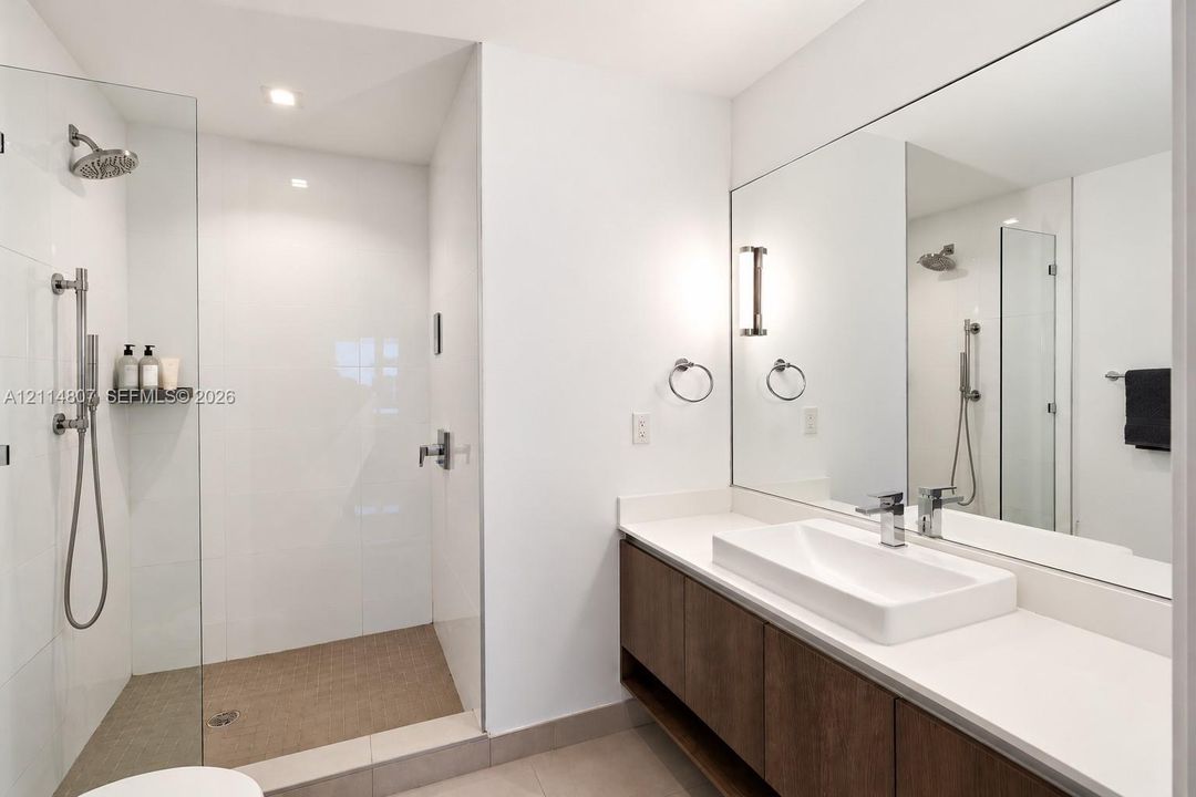 Walk-in shower with frameless glass enclosure, rainfall showerhead, and handheld wand, paired with a floating vanity featuring a rectangular vessel sink and countertop