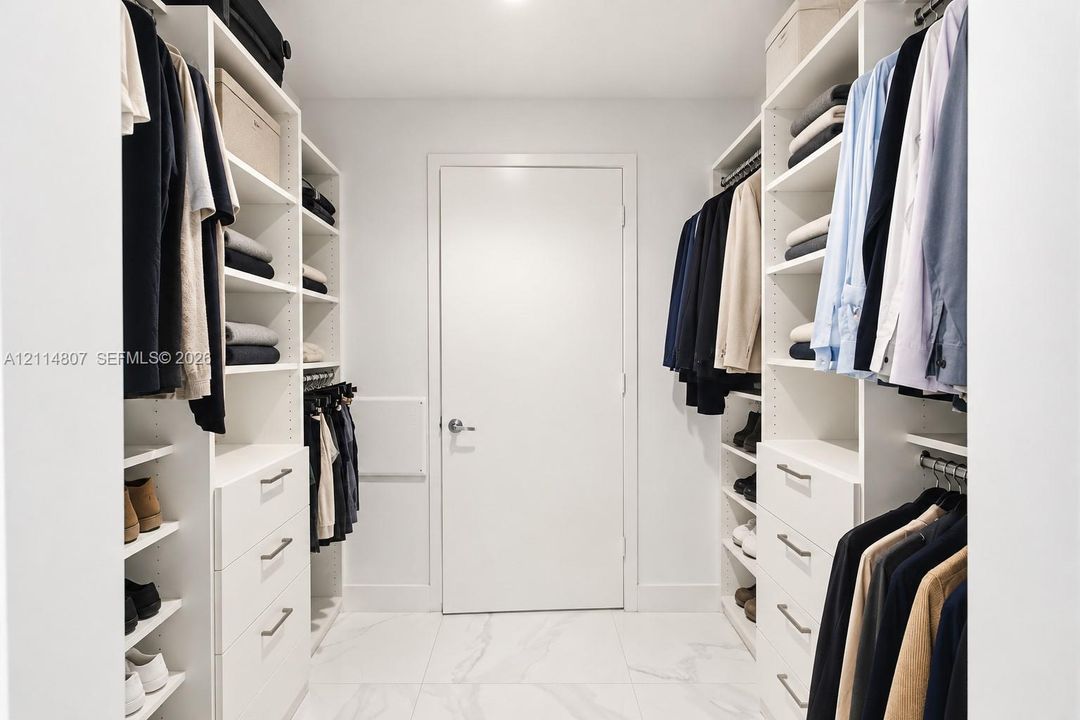 Custom walk-in closet featuring white built-in shelving, integrated dresser drawers with metal hardware, and white tile flooring with subtle veining