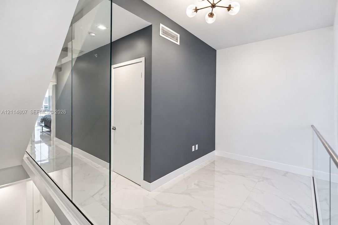 Interior landing featuring large-format tile flooring with marble-style veining, frameless glass panel railings, a charcoal accent wall, and a multi-arm sputnik-style ceiling light fixture