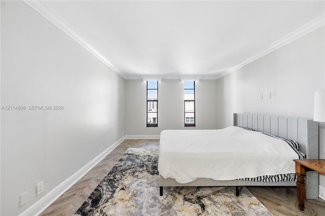 Herringbone-patterned wood-finish flooring, neutral wall tones, crown molding, and dual tall windows
